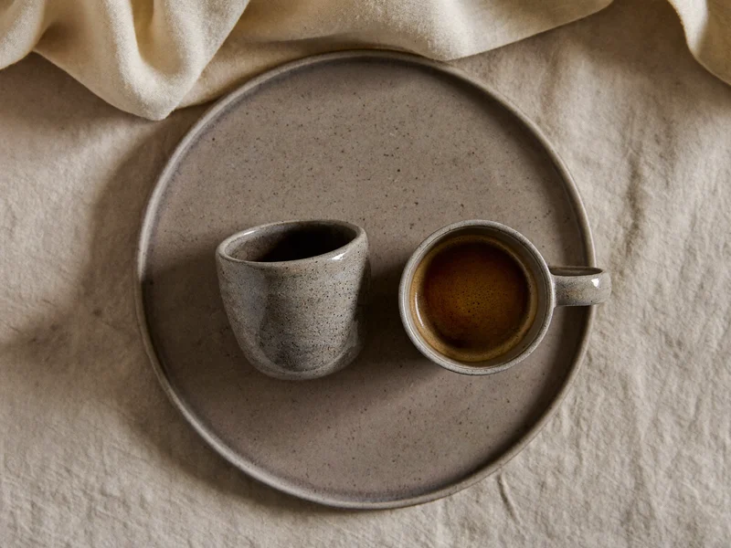 Stentøjsskål og espressokop arrangeret på naturligt linned set oppefra